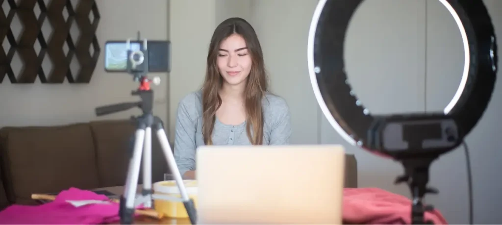 A woman streaming and sitting in front of a laptop with a camera
